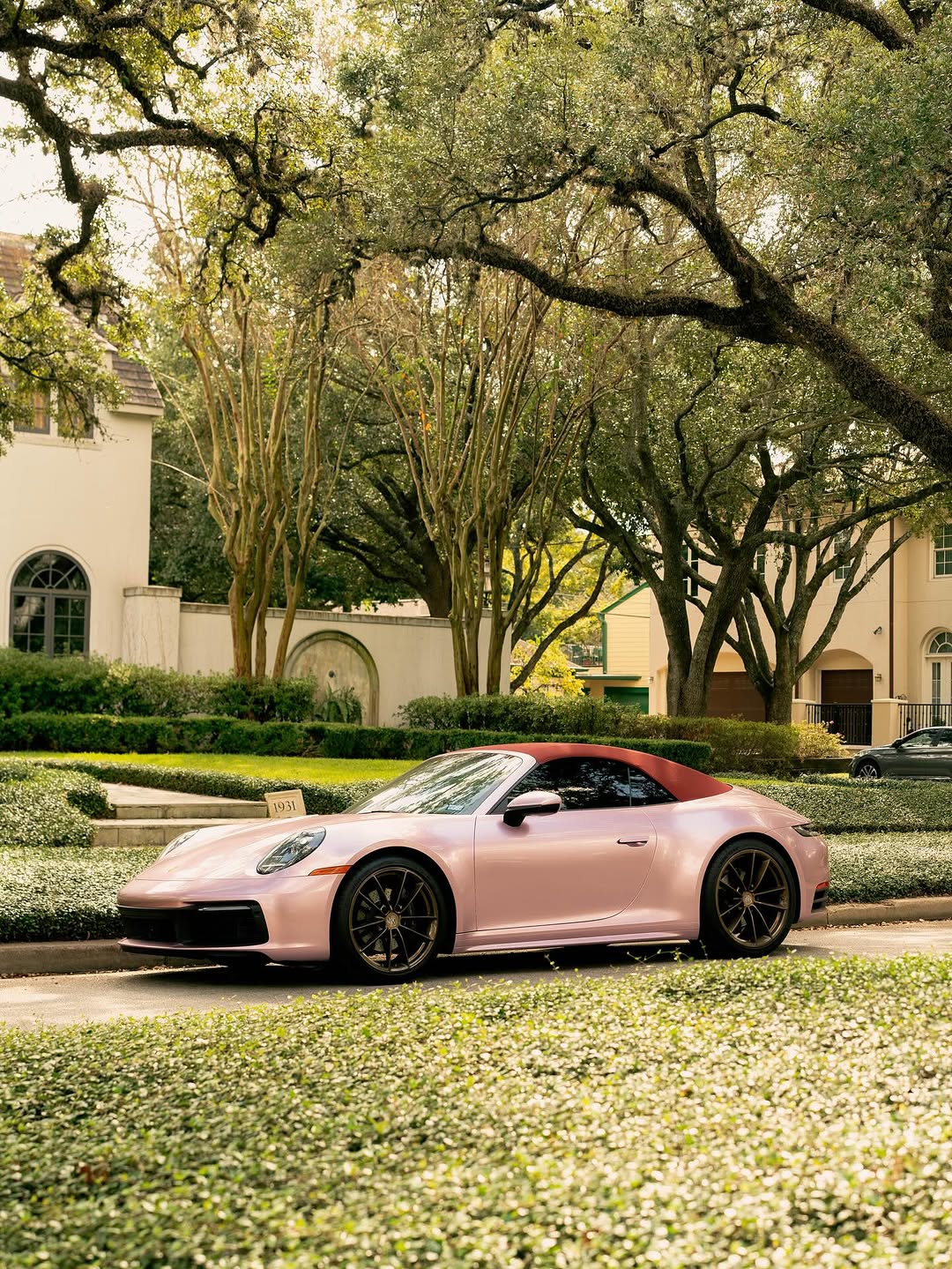 A pink Porsche convertible parked on a tree-lined residential street